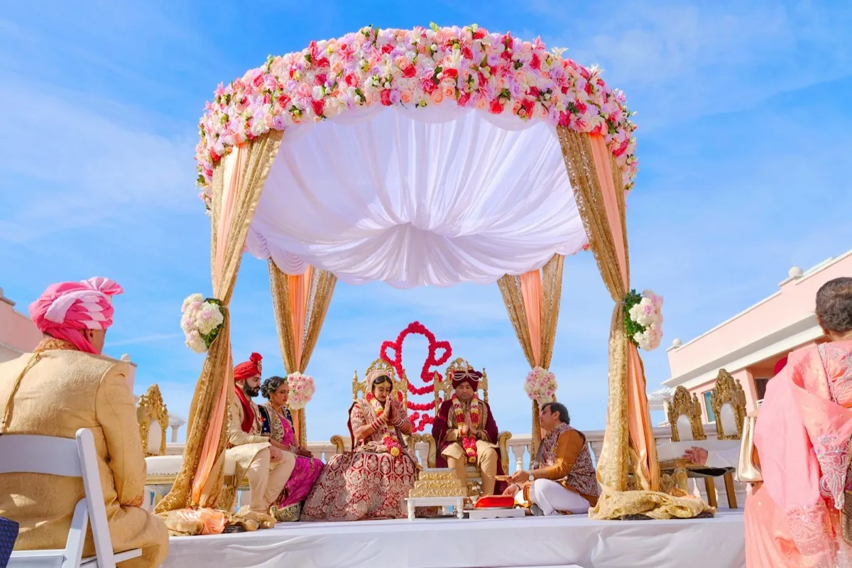 A couple seated under a flower-covered mandap during the wedding ceremony